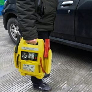 4v1 LED 12V booster 900A zaganjalec Jump Starter polnilec in kompresor 31 a person holding a yellow box with a red and black battery